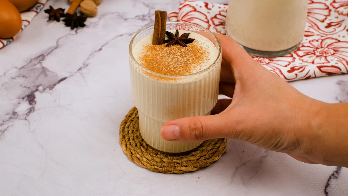 Low-carb eggnog served in a see-through glass with cinnamon sticks, star anise, and a sprinkle of cinnamon and nutmeg powder.