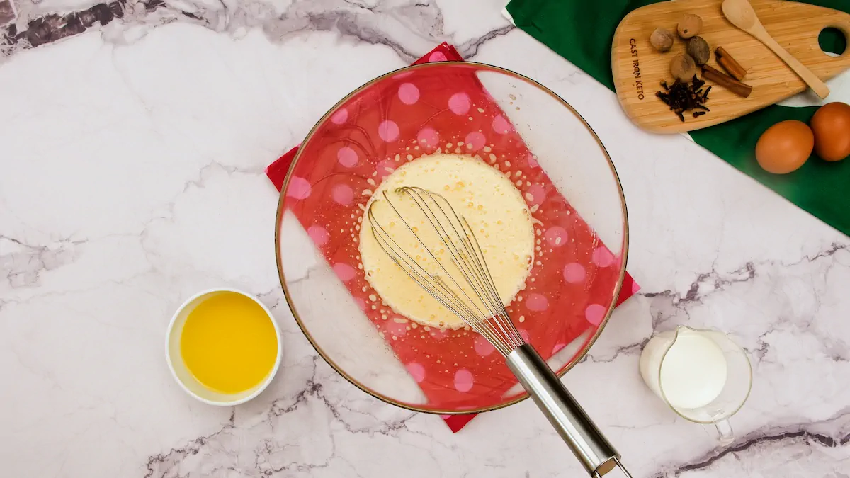 A mixing bowl with a mixture of whisked eggs and granulated erythritol alongside bowl with melted butter and heavy cream.