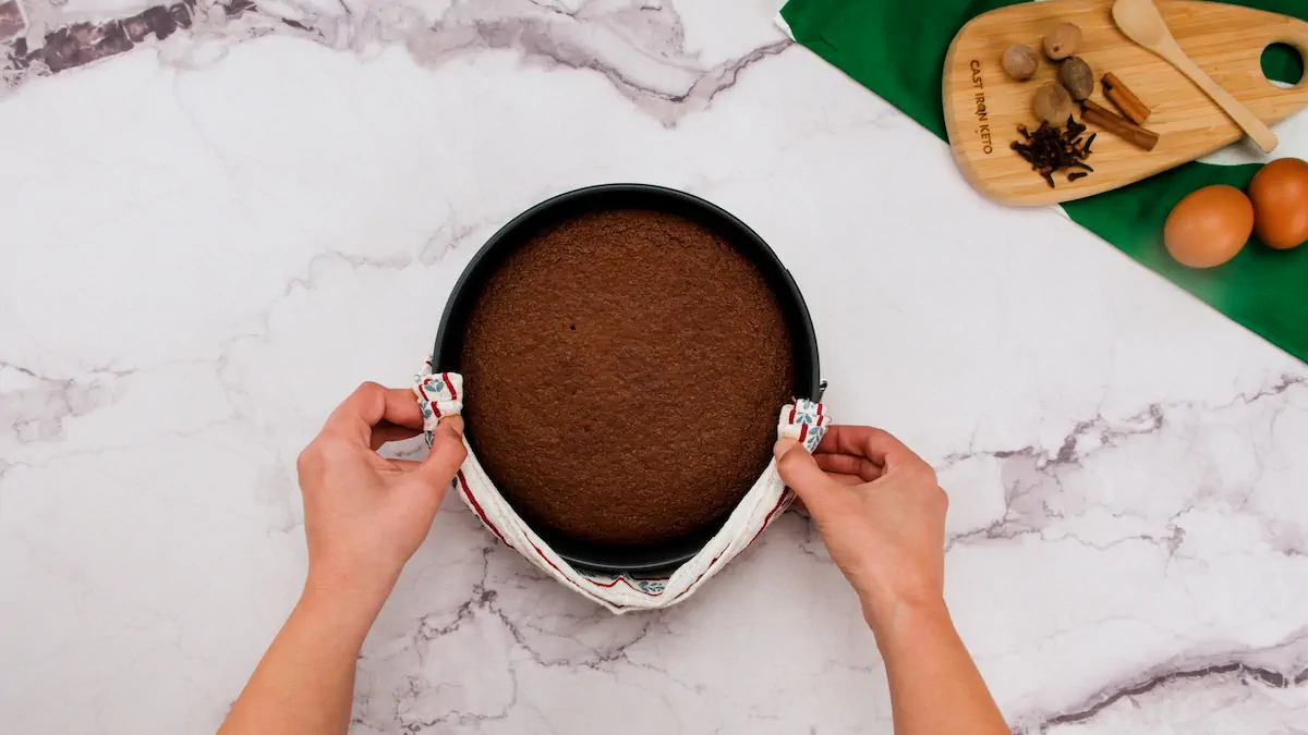Freshly baked keto gingerbread cake on a kitchen counter, held by two hands using a kitchen towel.