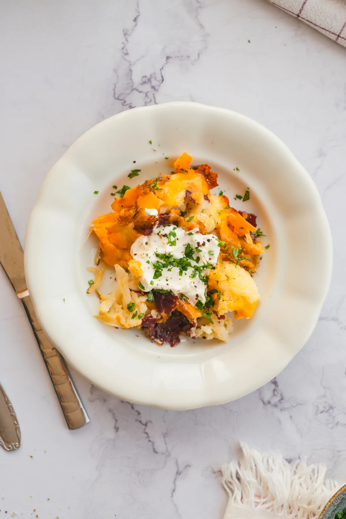 A close-up shot of loaded cauliflower casserole served with a dollop of sour cream and adorned with fresh herbs.