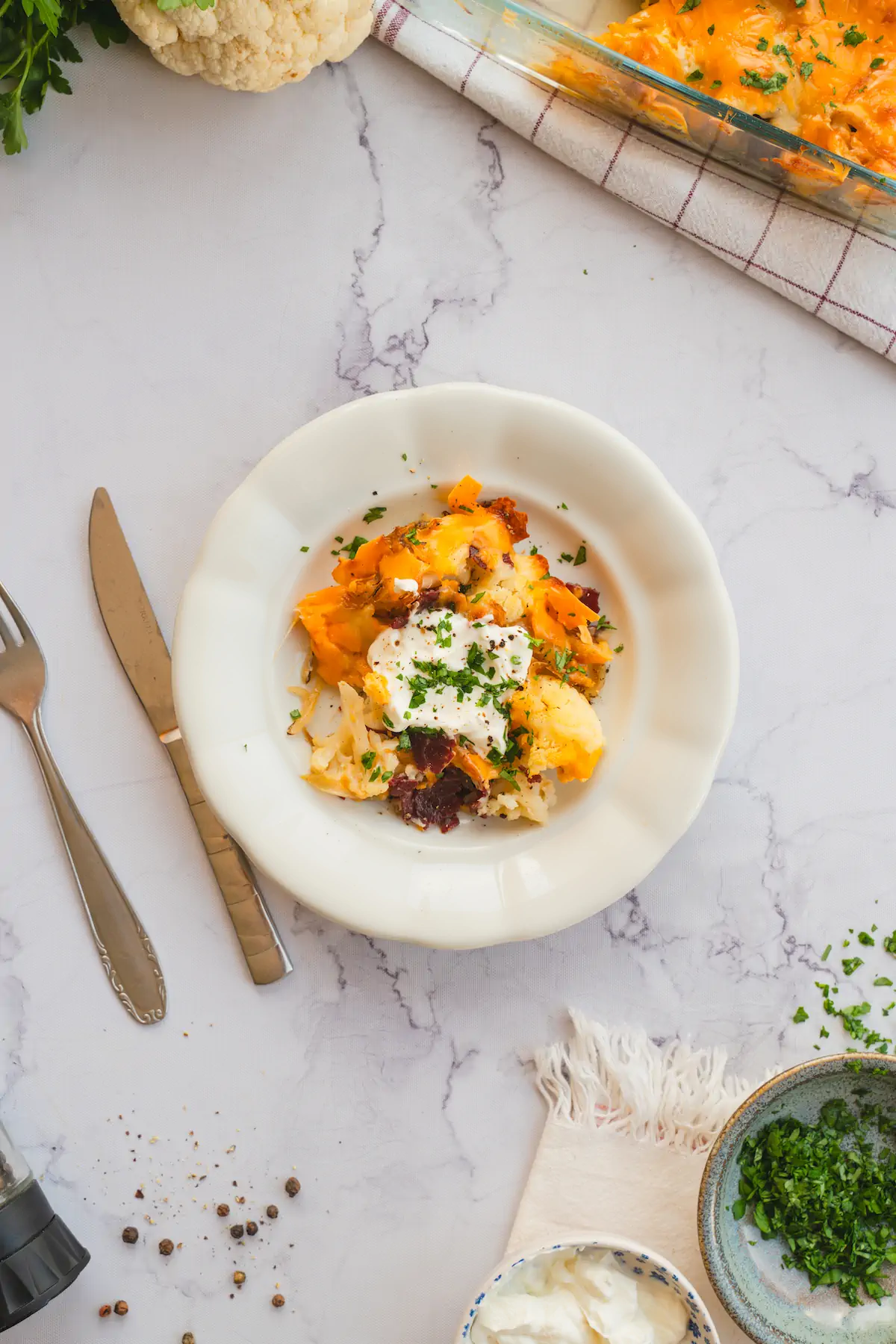 Keto-loaded cauliflower casserole served with sour cream and finished off with fresh herbs.