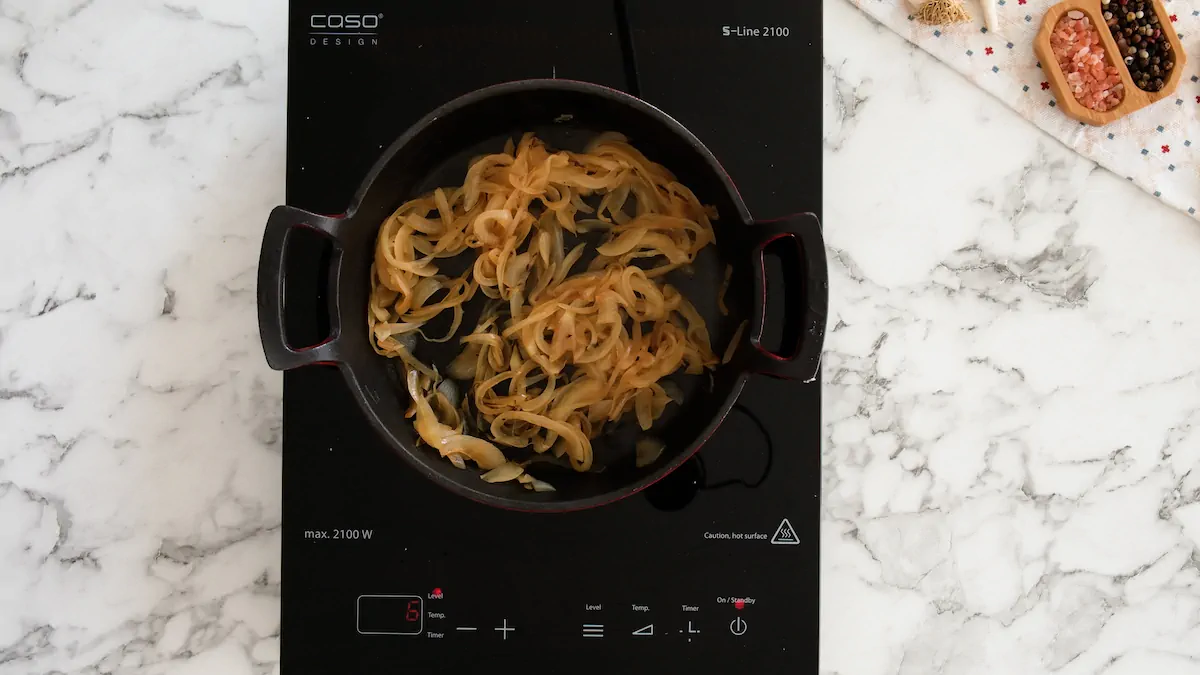 Caramelizing the sliced onions in a cast-iron skillet on an induction stove top.