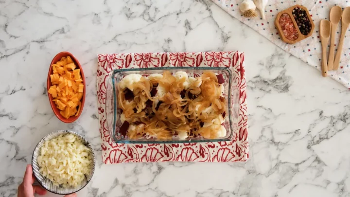 Loaded cauliflower casserole ready to be baked alongside cheddar and mozzarella cheese in separate bowls.