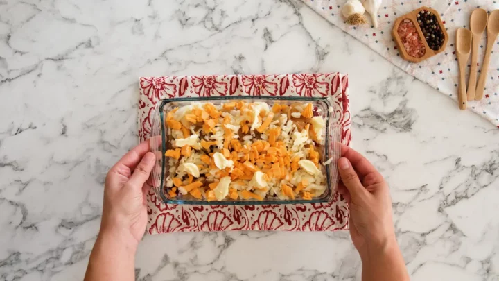 Two hands holding the loaded cauliflower casserole ready to be popped in the oven.