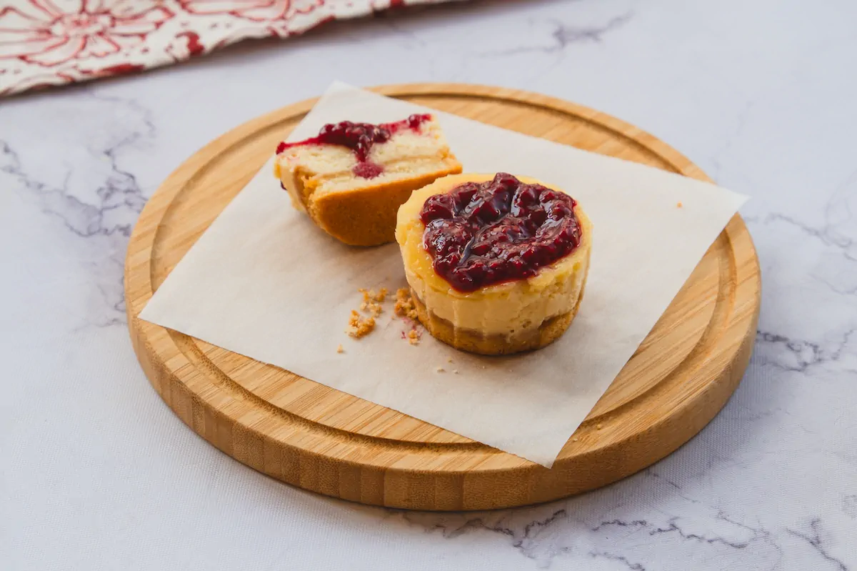 Gluten-free mini cheesecake bites topped with raspberry jam, with one cut in half to reveal the texture.