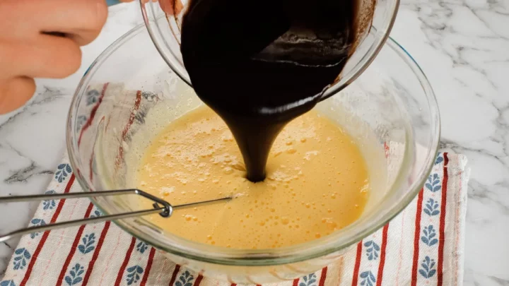 Pouring the chocolate mixture into a bowl with the egg and erythritol mix.