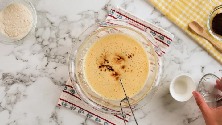 The mixture of egg and chocolate in a transparent bowl in the center alongside coconut flour, peppermint extract and sea salt.