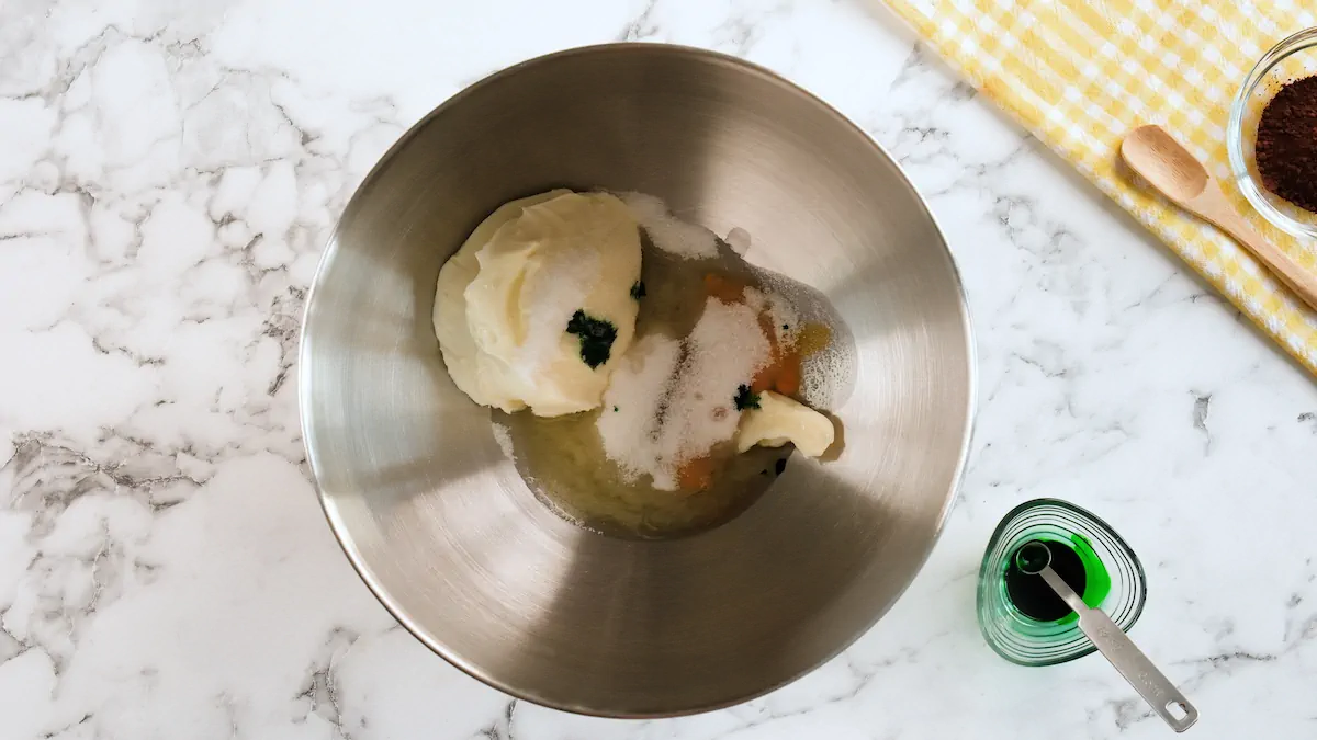All the ingredients for the filling of mint brownies put in a stainless steel bowl alongside a bowl with green food color.