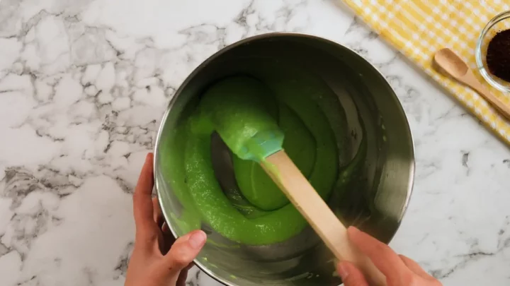 Checking the whisked cream cheese filling with a silicone spatula in a stainless steel bowl of a stand mixture.