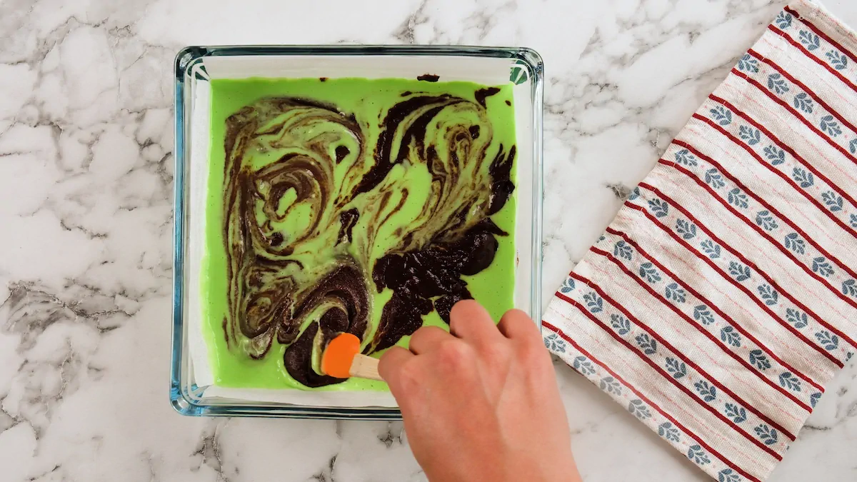Mixing the mint brownie batter in a glass baking dish with a silicone spatula.