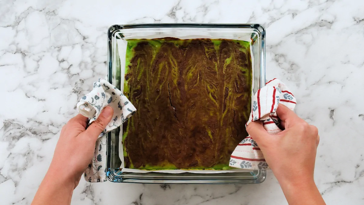 Two hands holding freshly baked keto mint brownies with kitchen towels.
