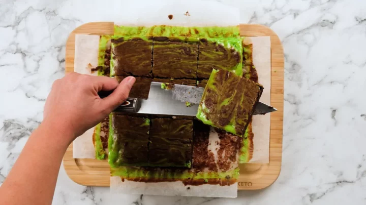 Mint brownies cut into squares using stainless steel knife and holding a piece with the knife.