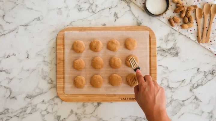 Creating a design on the no-bake coconut cookies using a fork on a wooden board lined with parchment paper.