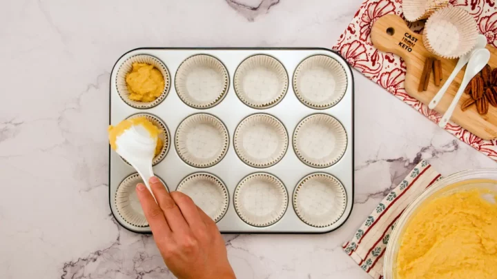 Putting the almond flour muffin batter into the muffin tray lined with muffin liners.