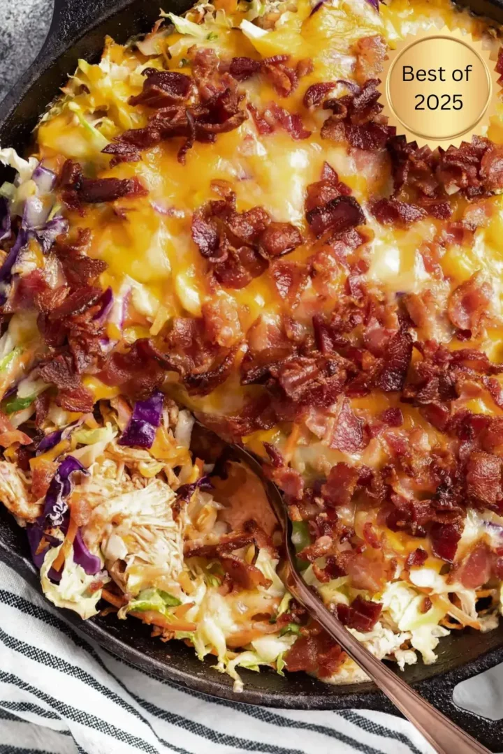 Close-up of a cheesy chicken and cabbage skillet topped with crispy bacon and melted cheese, with purple and green cabbage visible underneath