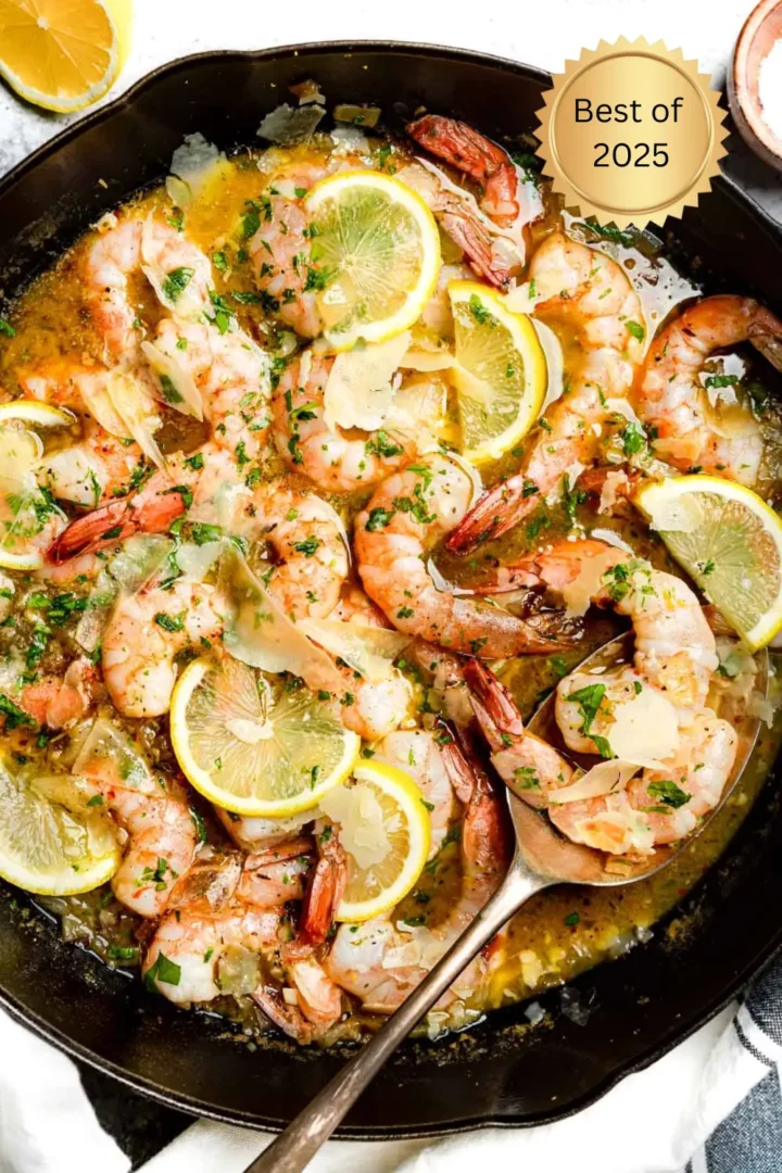 Garlic butter shrimp cooked in a skillet with lemon slices, fresh herbs, and parmesan shavings in a rich, buttery sauce.