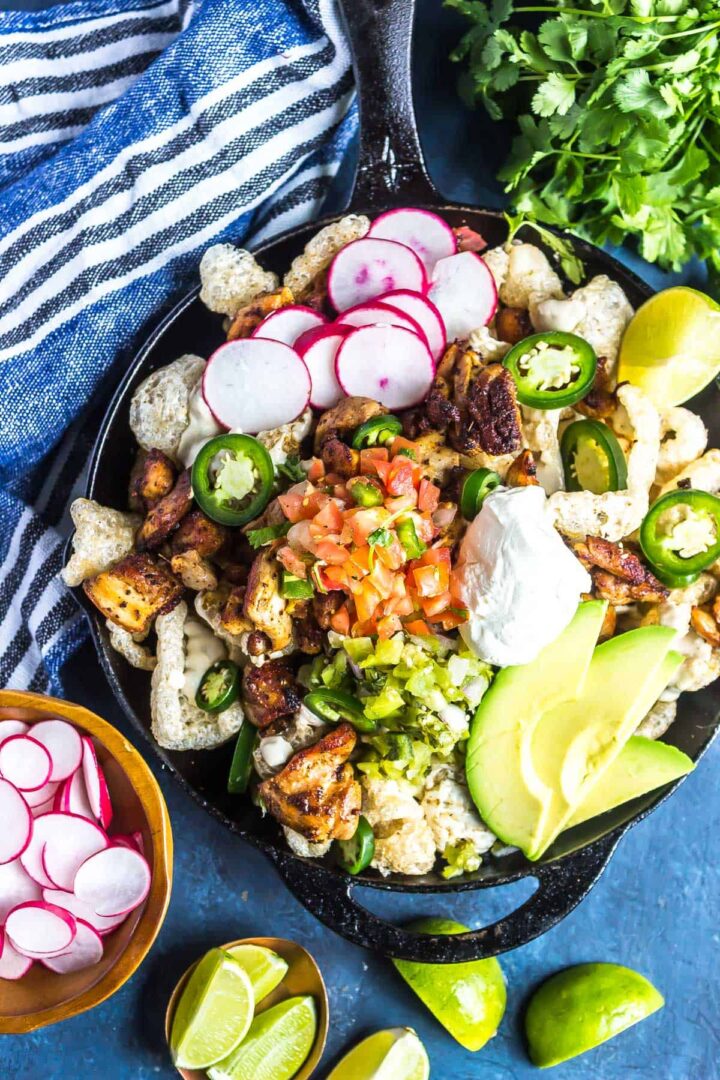 Keto Nachos in a cast iron skillet topped with salsa, avocado, sour cream, radishes, and more
