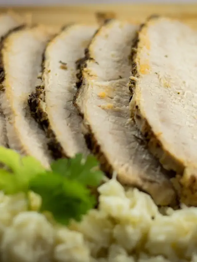 Plating slow cooker pork loin with mashed cauliflower on a wooden board.