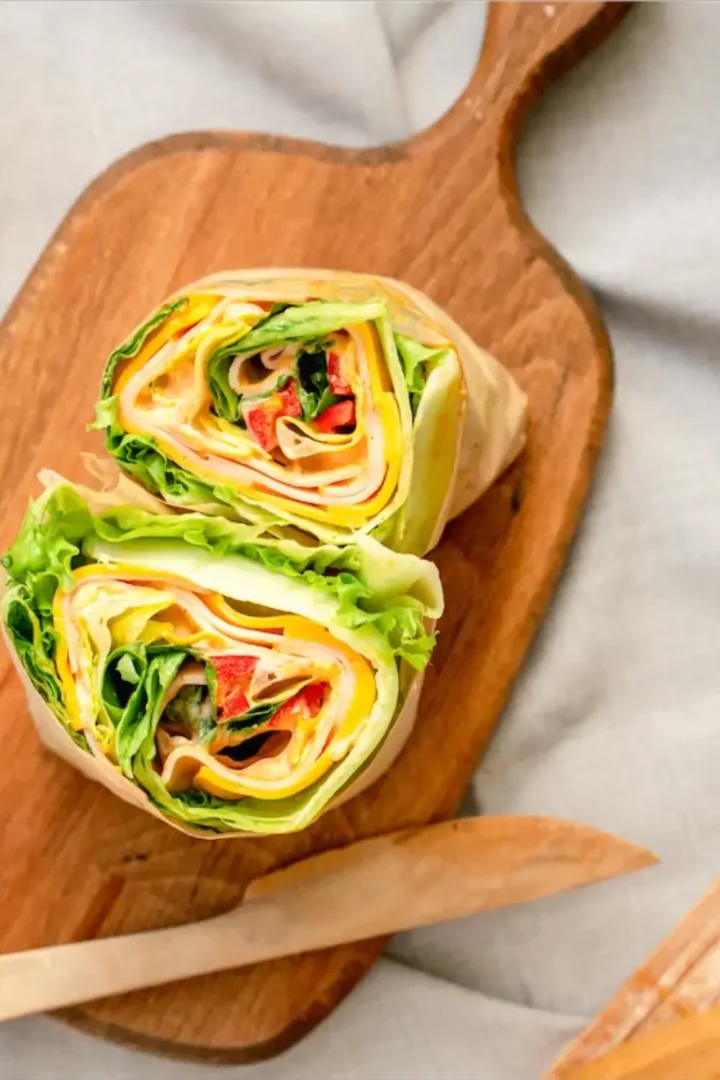 Keto lettuce wrap made with layered lettuce leaves, smoked turkey, cheddar cheese, red bell pepper, mint, and herb mayonnaise, rolled tightly on parchment paper