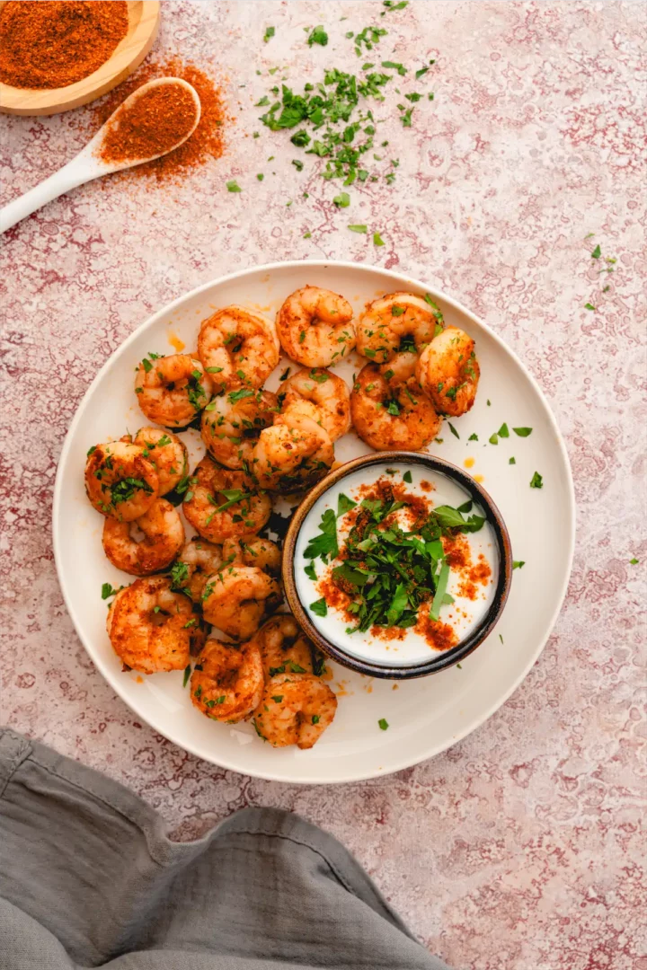 Keto Cajun shrimp on a white plate accompanied by a small bowl of dip ready to be served